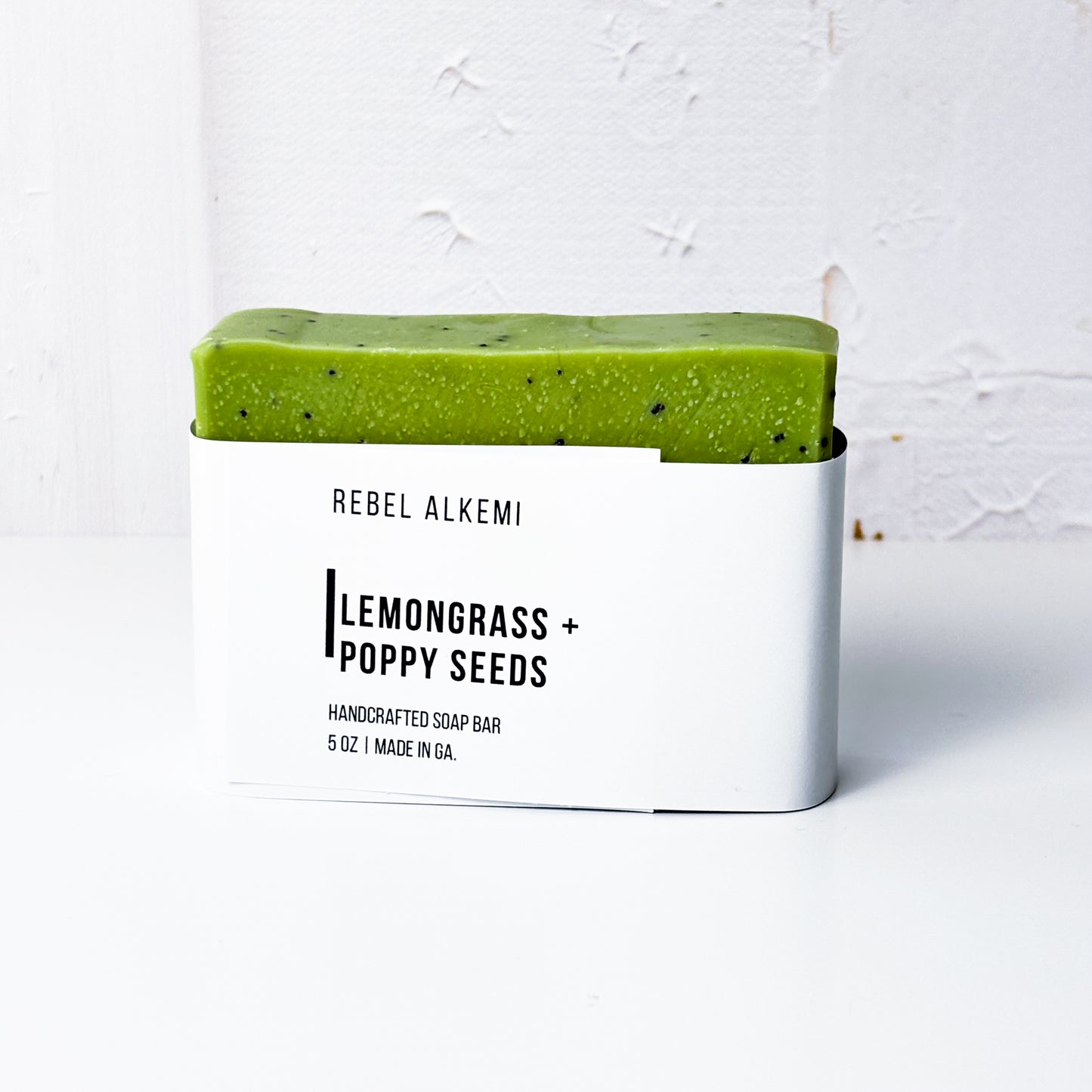 Lemongrass and Poppy Seed soap bar in a white container with 'Rebel Alkemi' branding on a light gray background
